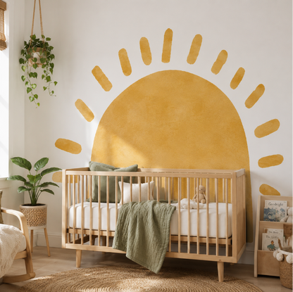 A wooden baby crib with white bedding and a sage green throw blanket, styled in a bright nursery with a large yellow sun wall mural behind it.